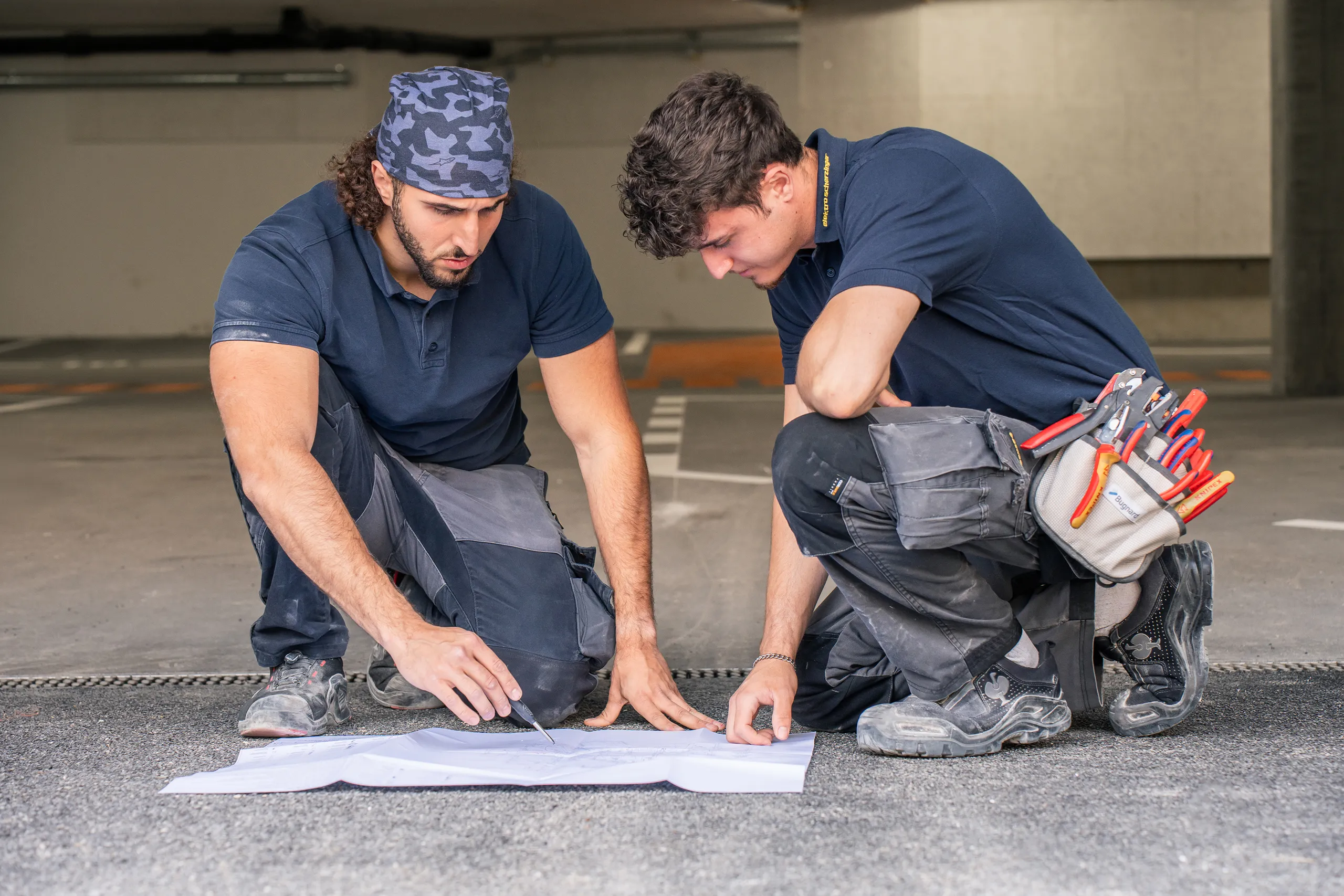Zwei Elektriker der elektro scherzinger ag prüfen einen Installationsplan in einer Tiefgarage