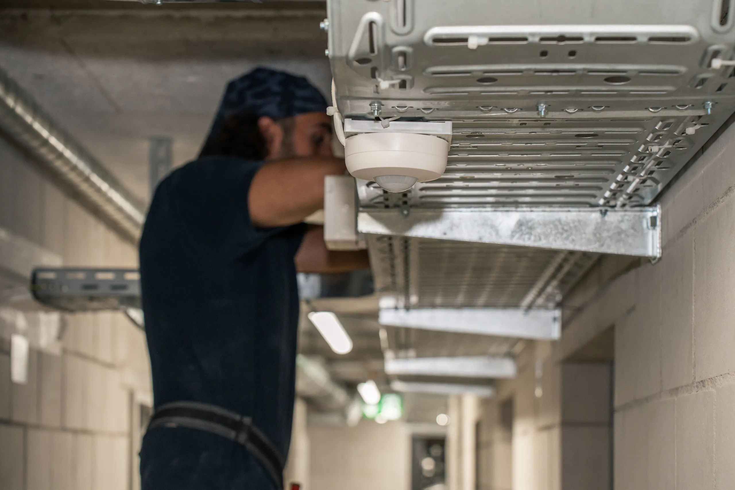 Elektriker der elektro scherzinger ag installiert einen Brandmelder an der Deckenkonstruktion